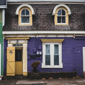 Vivid purple and yellow facade of a Victorian-style house with distinctive arched windows and detailed trim.