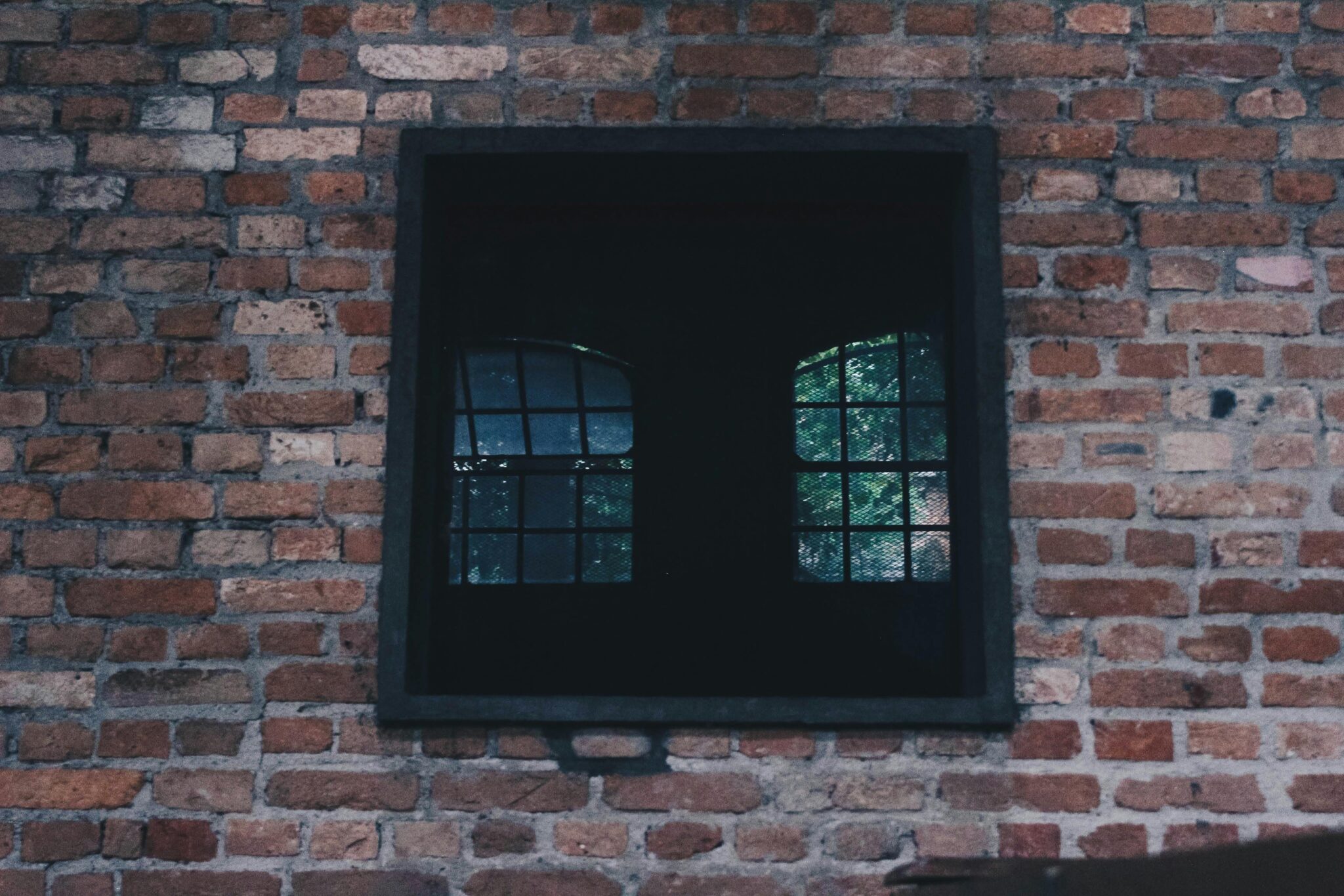 A rustic brick wall featuring a vintage iron window located in Mooca, São Paulo.