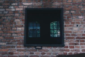 A rustic brick wall featuring a vintage iron window located in Mooca, São Paulo.